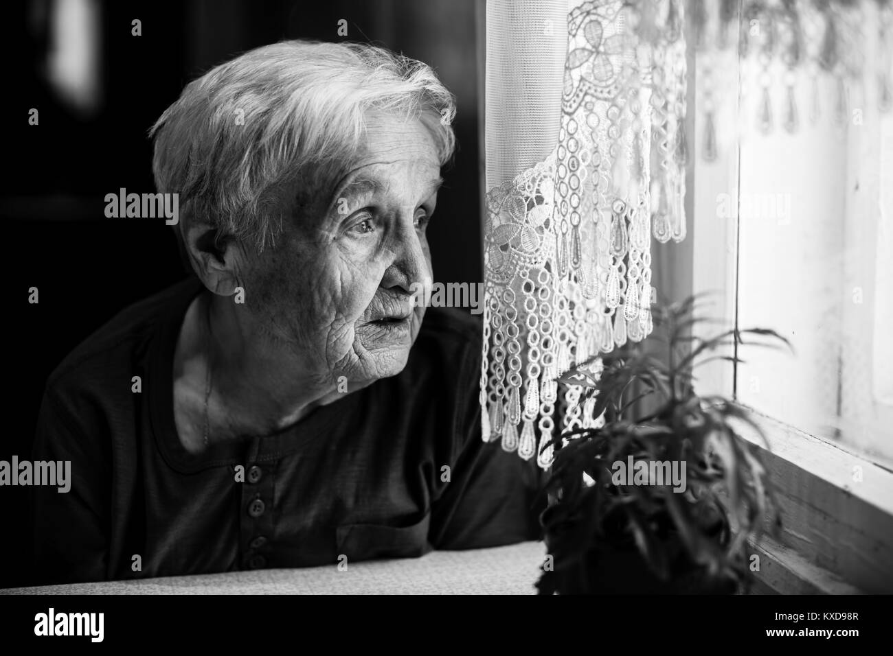 Elderly woman looking sad out the window. Stock Photo