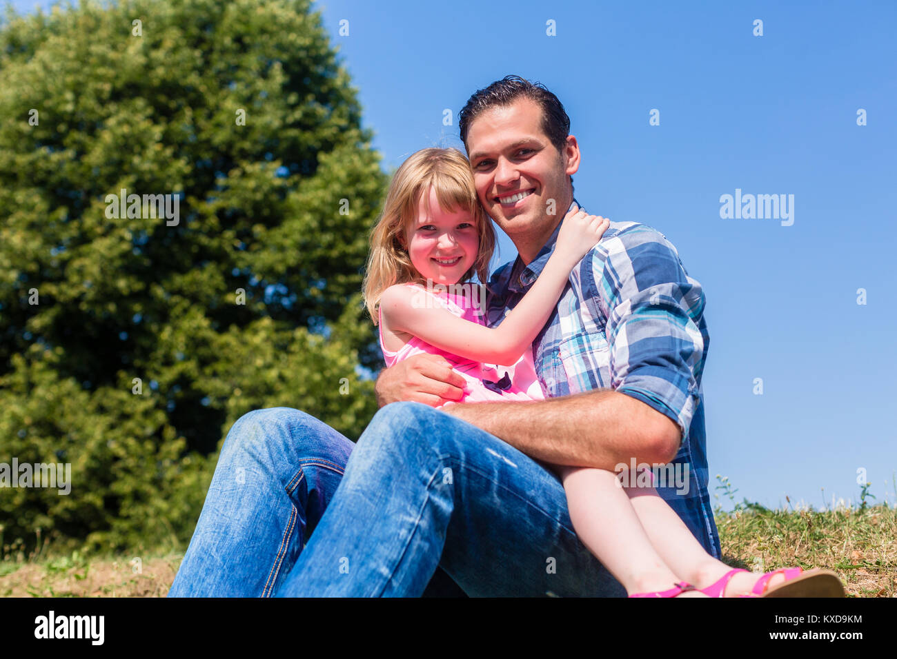 Girl on dads lap sitting on meadow or in field Stock Photo