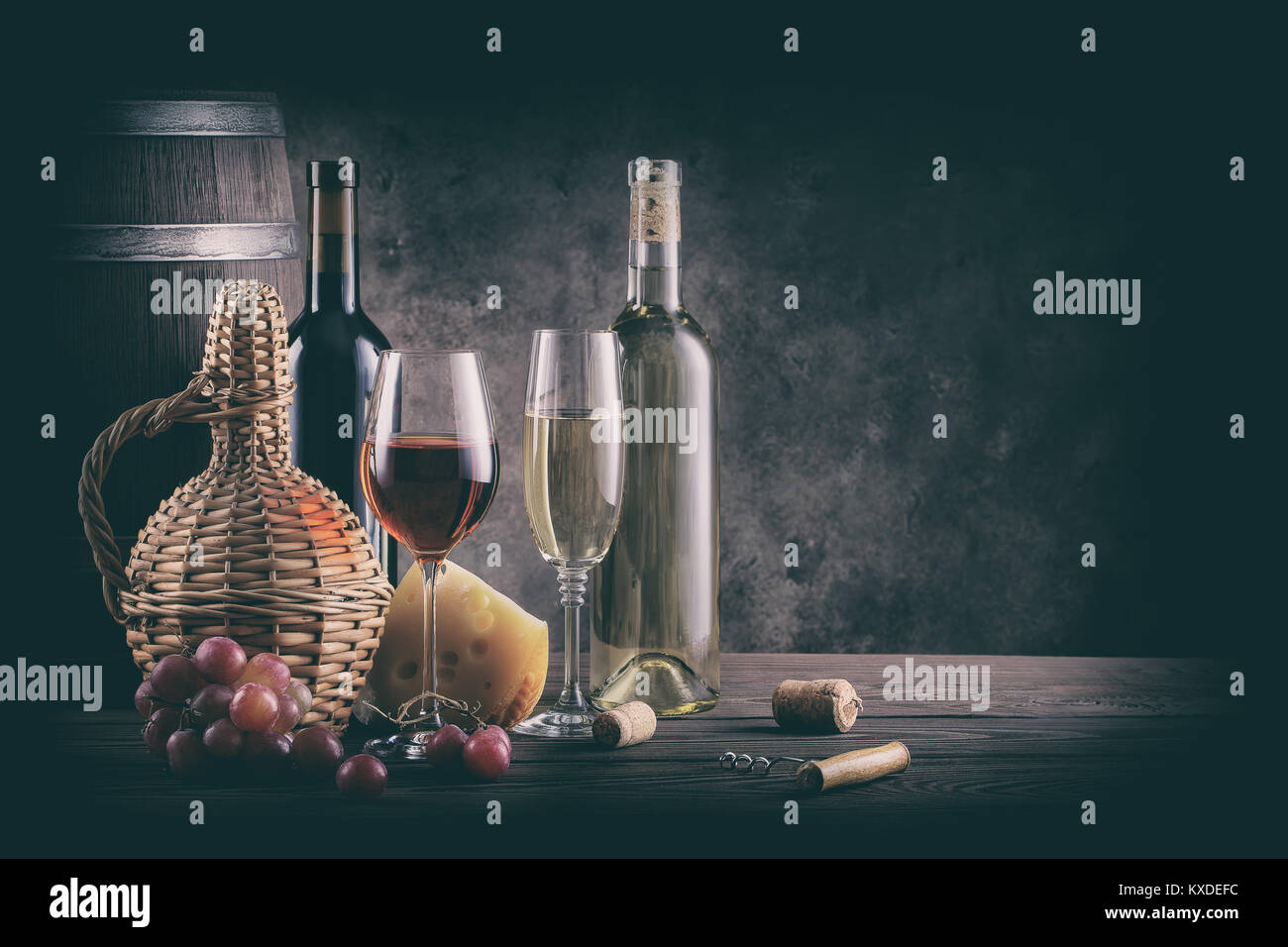 Wine still life on wooden table. Processing for vintage. Bottles, glasses, barrel and grapes with cheese on a wooden table. Stock Photo