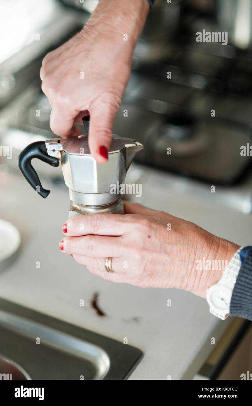An elderly woman prepares an espresso using a traditional Bialetti espresso coffee machine Stock Photo
