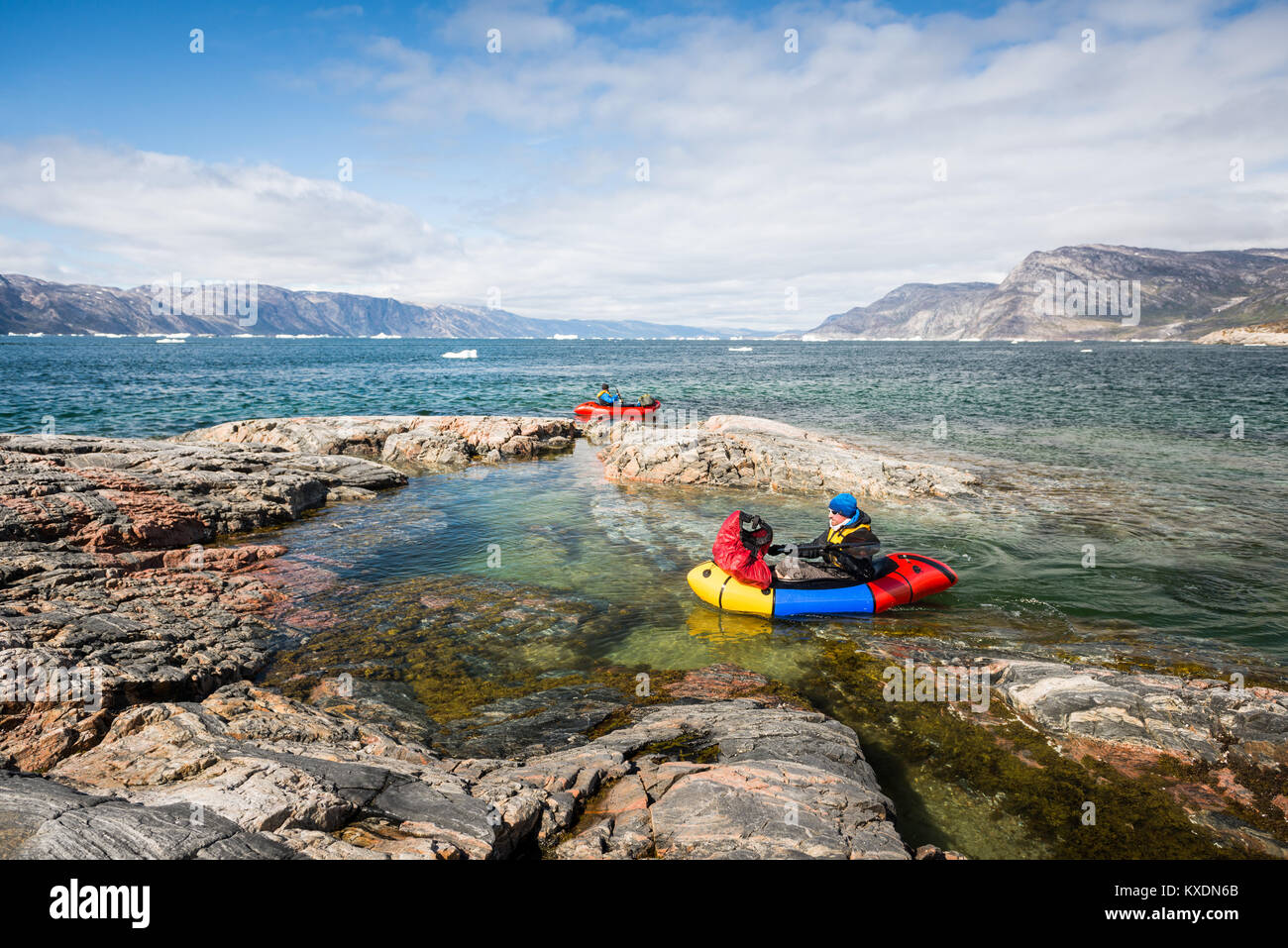 Two persons with packing trucks on fjord, rocks, behind mountains, Greenland Stock Photo