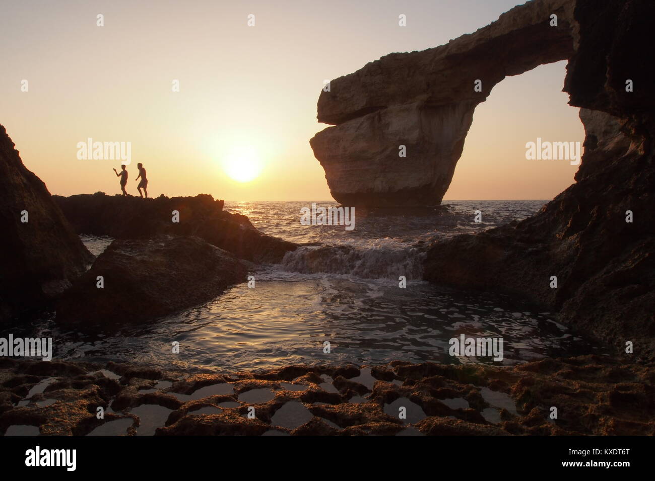 Toursists having fun in Dwerja Bay with the famous Azure Window in the background at sunset, Gozo, Malta Stock Photo