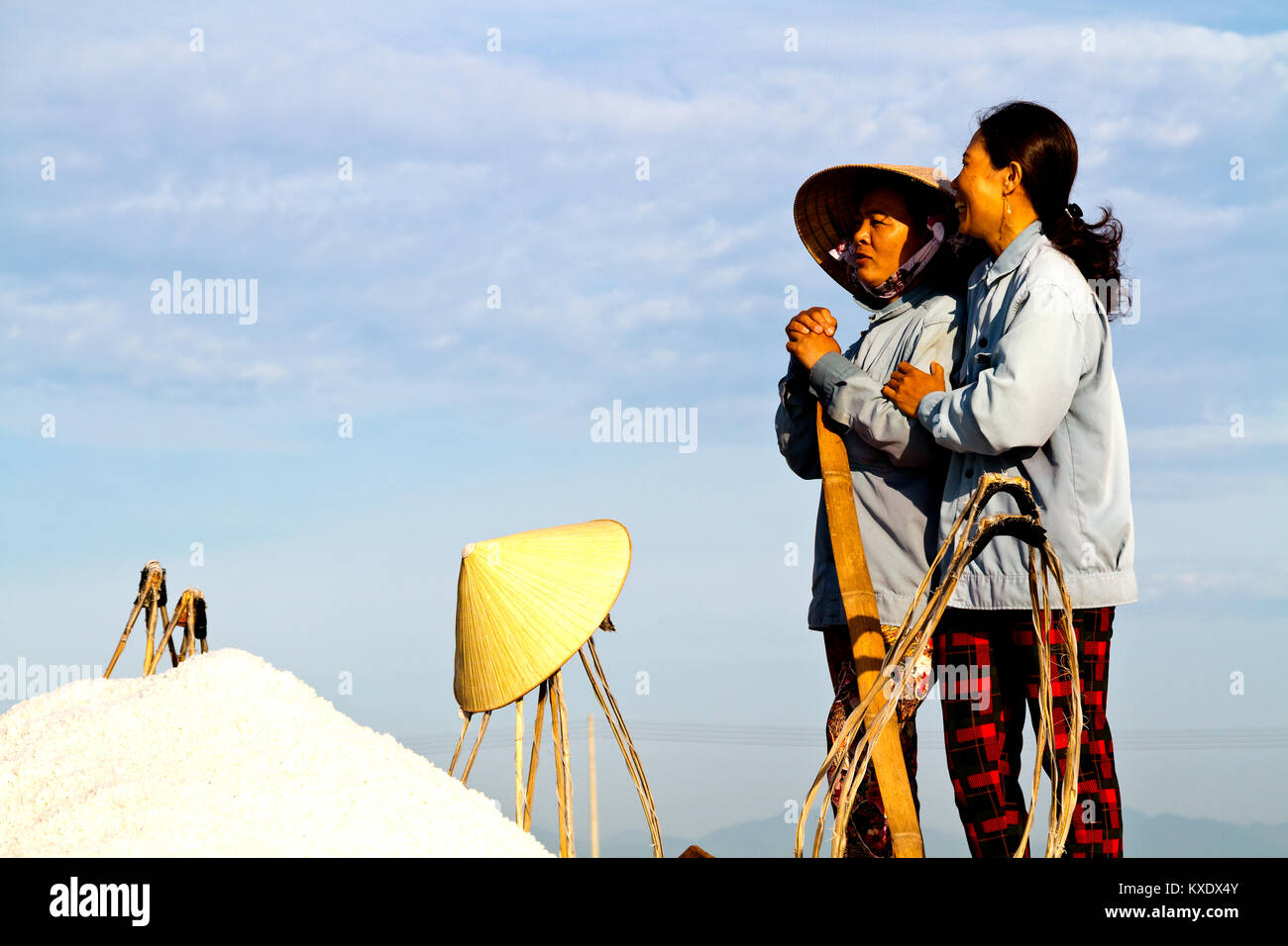 Relaxing female workers harvesting salt from salt water ponds close to DocLet, Vietnam. They start work long before sunrise to avoid most of the heat Stock Photo