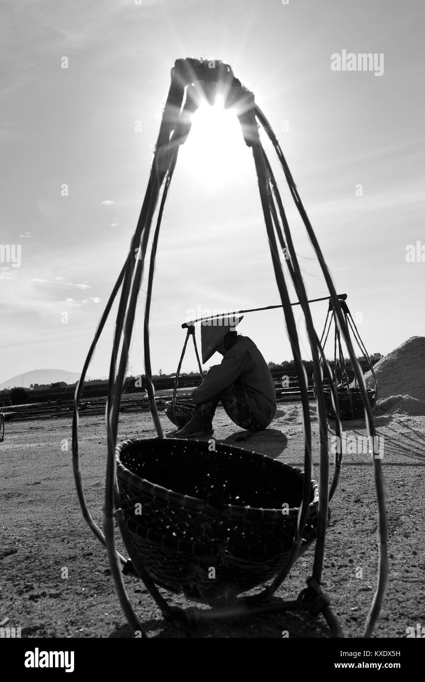 A tired female worker harvesting the salt from salt water ponds near DocLet, Vietnam. They start work long before sunrise, to avoid most of the heat Stock Photo
