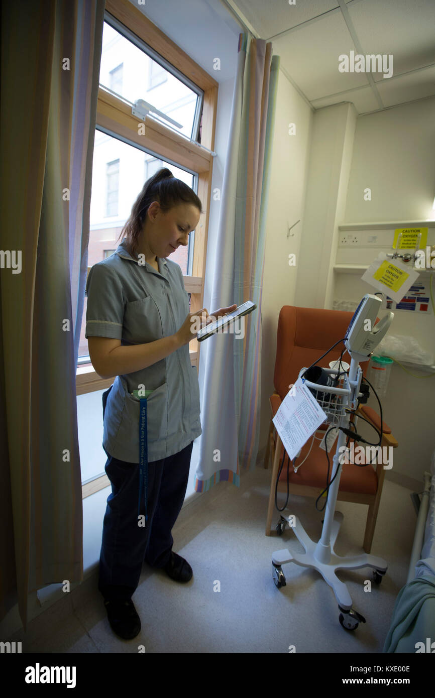Staff nurse Charlotte Howden, inputting data into an iPad on a ward at Whiston Hospital in Merseyside. The device is used to facilitate the Electronic Modified Early Warning System (EMEWS) which helps alert clinical staff to which patients require priority treatment at the hospital. The system, introduced at Whiston Hospital in 2016, allows staff to monitor and regulate patient care in a more efficient way than previous paper-based systems. Stock Photo