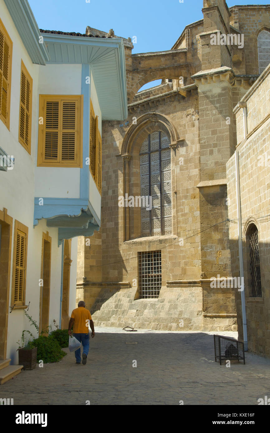 Local man walking down a small street with a mosque that used to be a church in the background, Cyprus Stock Photo