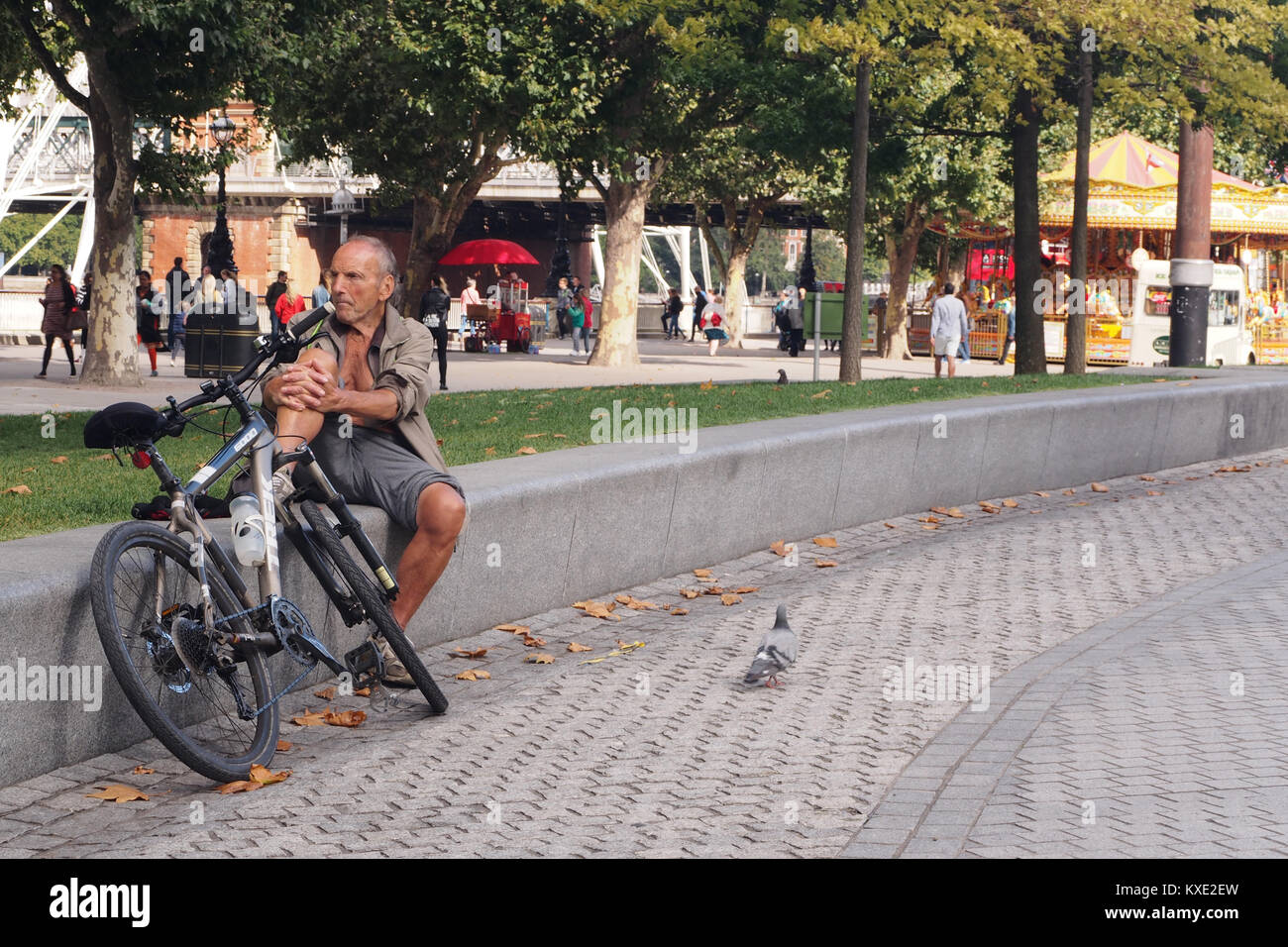 Man resting and crowd watching on a low wall with his push bike, near the London Eye Stock Photo