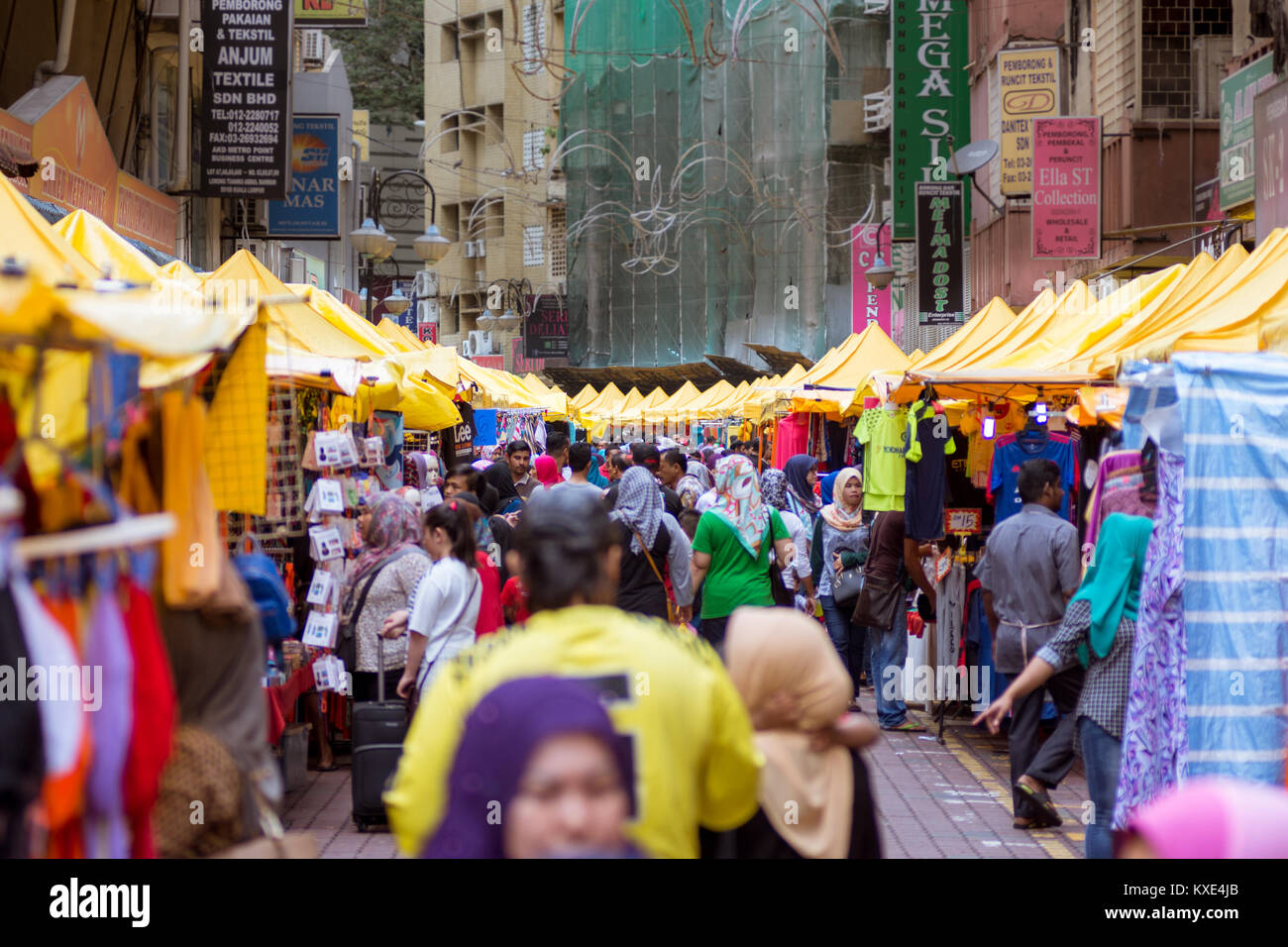 Blurred view of a busy daytime street market. Street busy with people and lined with yellow roofed stalls. Stock Photo
