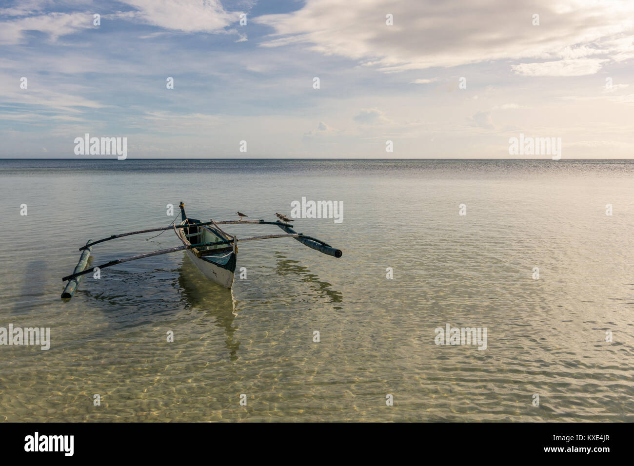A Filipino fisherman's basic pump boat floating empty on a still calm tropical sea with seagulls resting on its stabilizers. Stock Photo