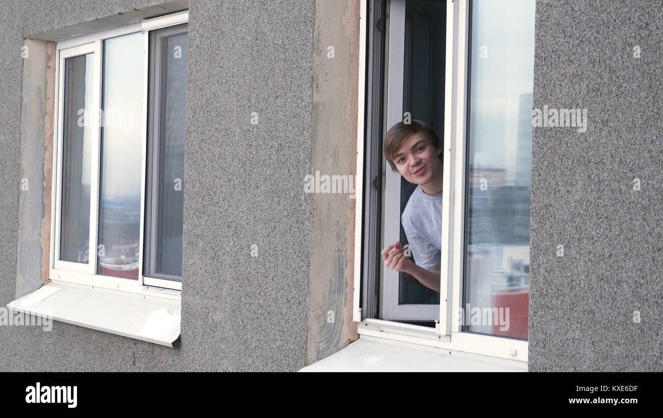 Young man smoking cigarette through the window of house. Man smoking by