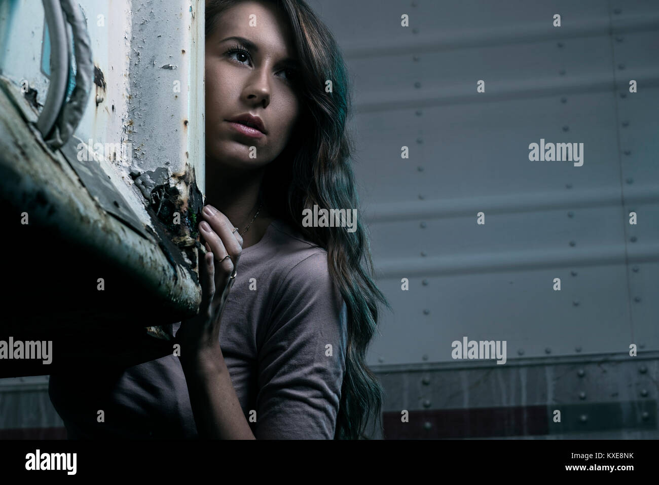 Young woman standing and hiding around semi trailers Stock Photo