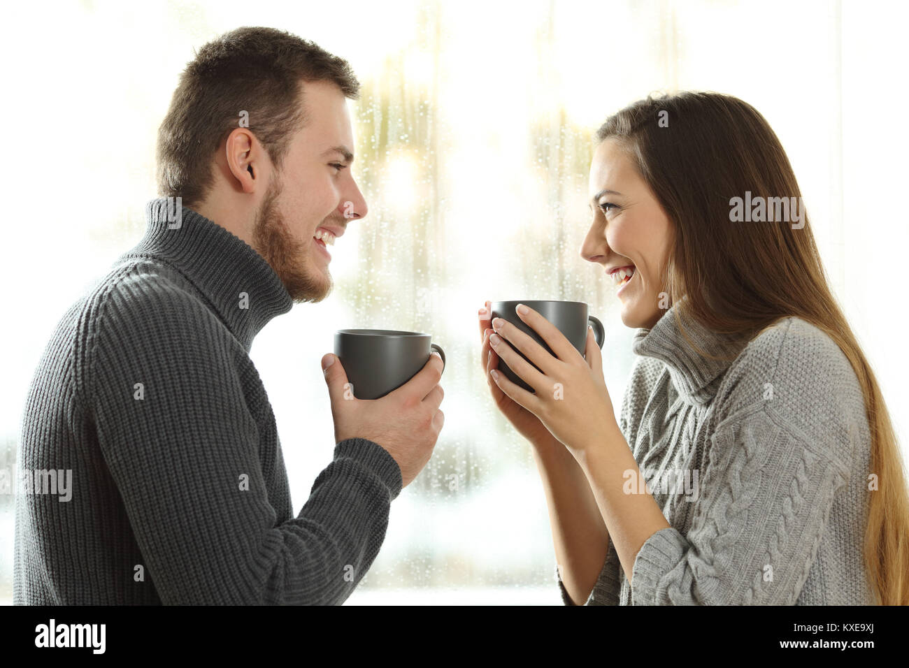 Side view portrait of a happy couple in love looking each other in a rainy day of winter at home Stock Photo
