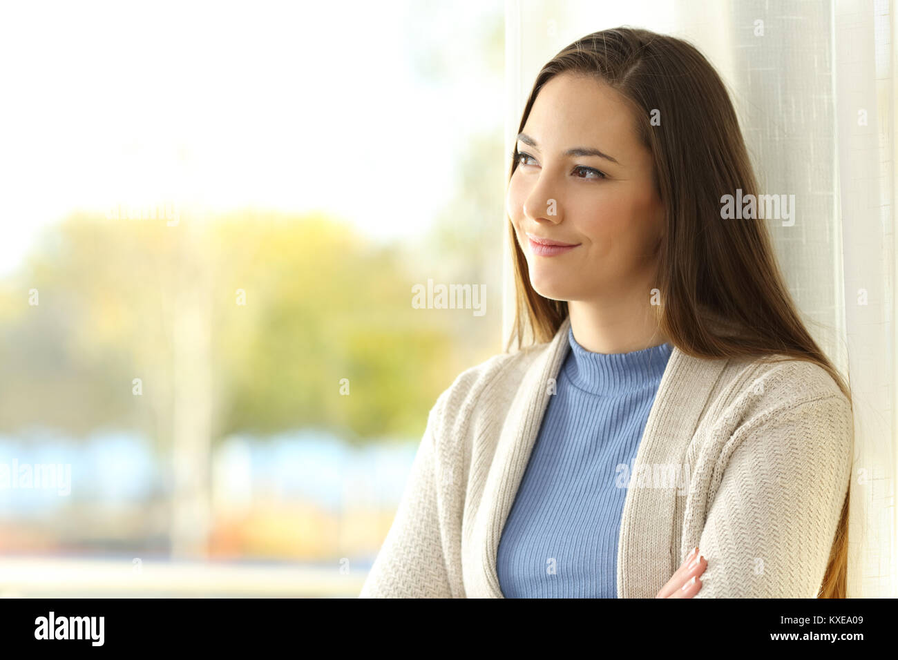 Portrait of a pensive tenant looking at side through a window at home Stock Photo