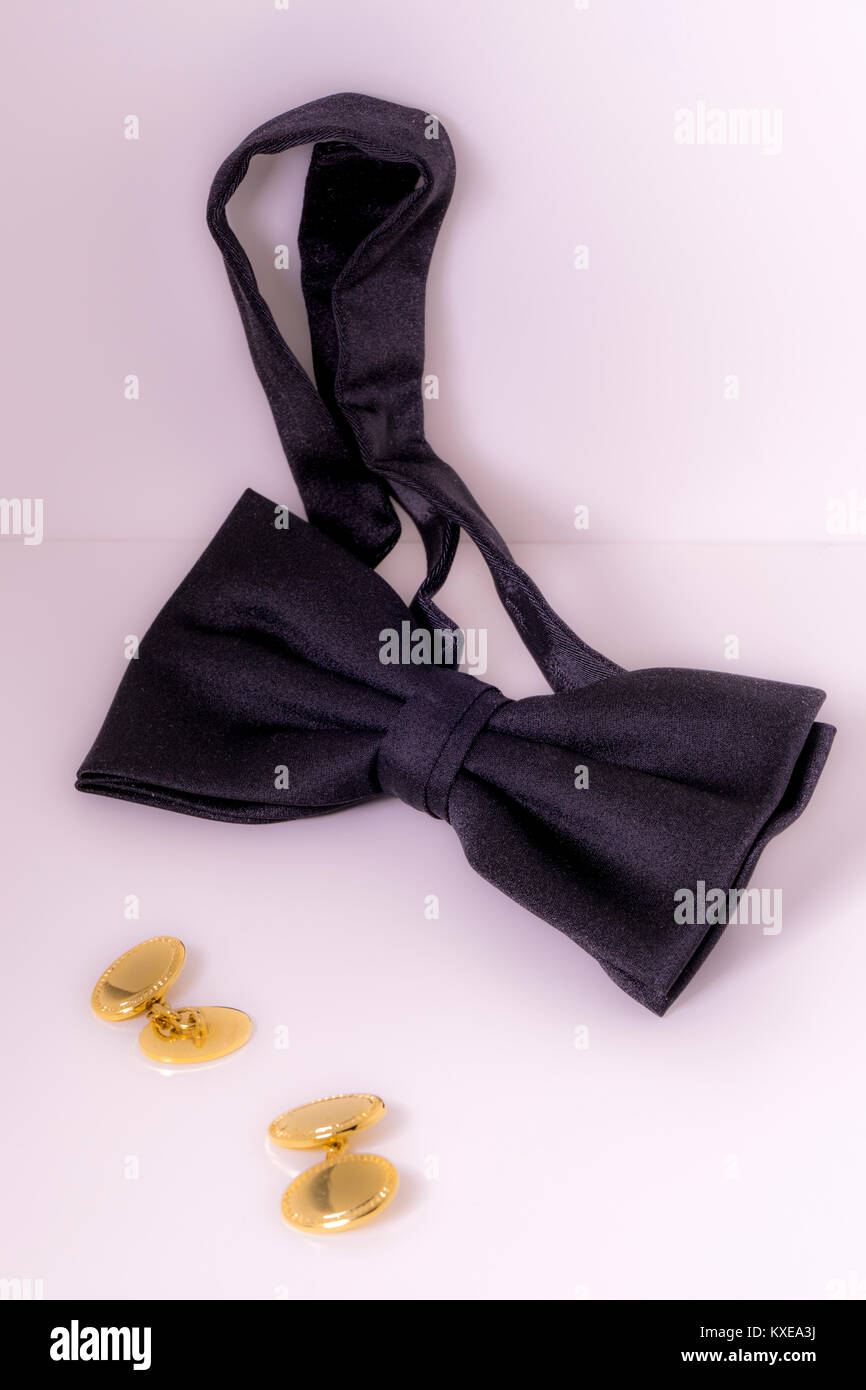 Bow tie, pre-tied classic design in black silk fabric, sitting alongside a pair of gold coloured cufflinks, ready for the more formal occasions. Stock Photo