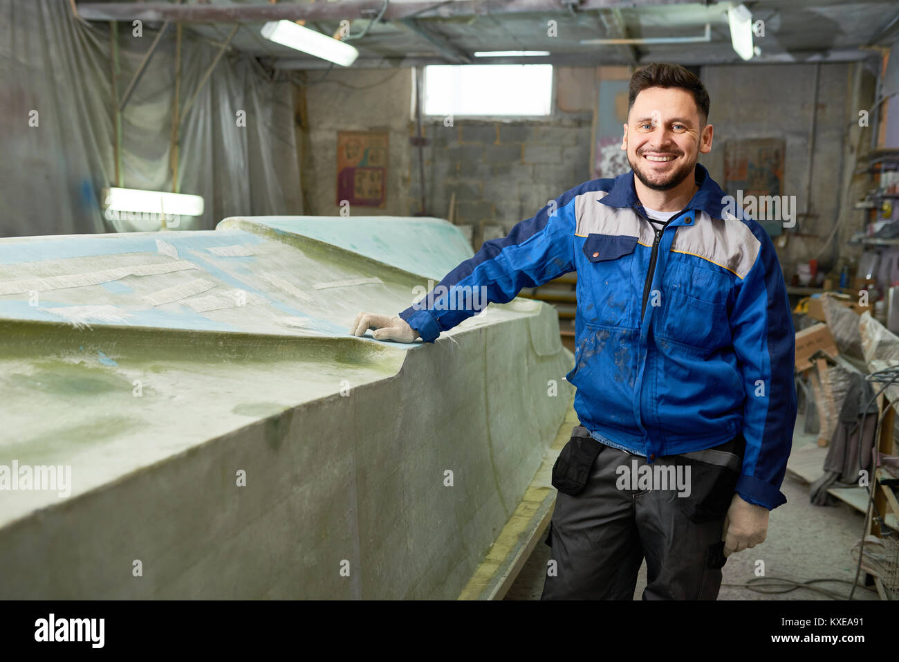 Portrait of modern mature man smiling happily at camera while posing in yacht workshop next to repaired boat , copy space Stock Photo