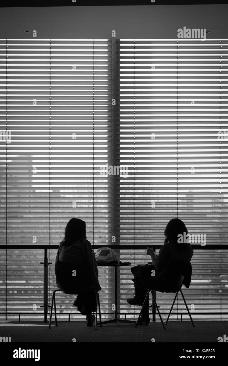 Two people sit in silhouette in large windows Stock Photo