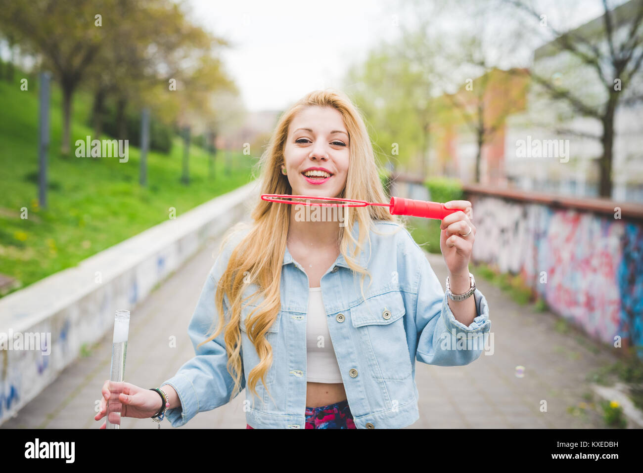 Young beautiful blonde caucasian girl playing with soap bubbles in the city park - childhood, carefreeness concept Stock Photo