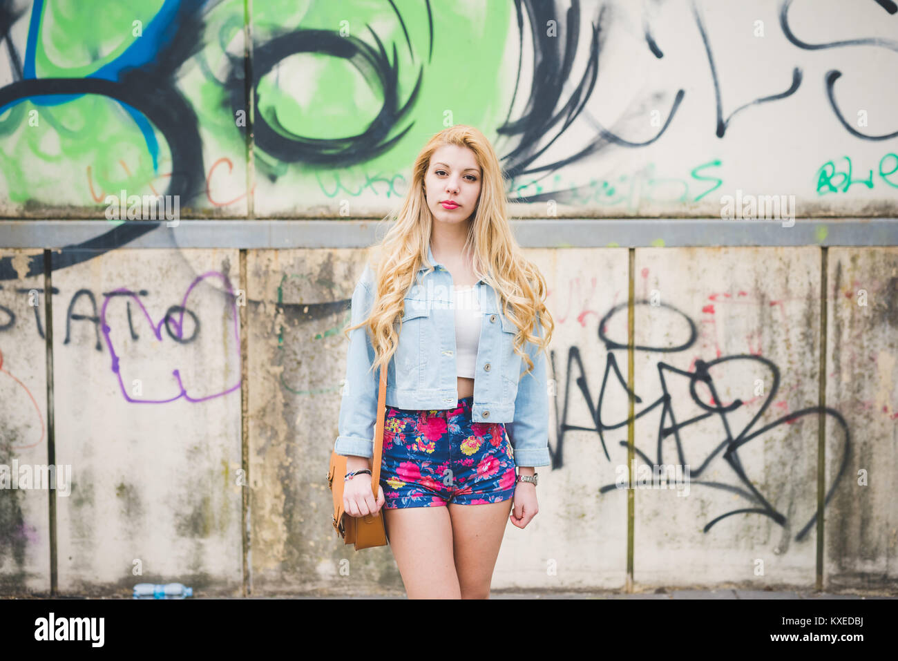 Young handsome blonde caucasian fashion girl posing leaning on a wall in the city suburbs Stock Photo