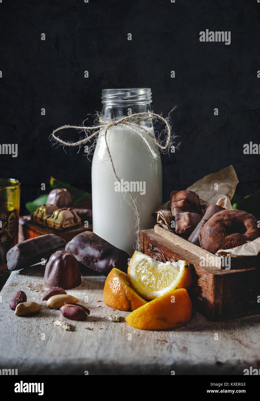 Milk in glass jar with orange and chocolate sweets. Dark wall at