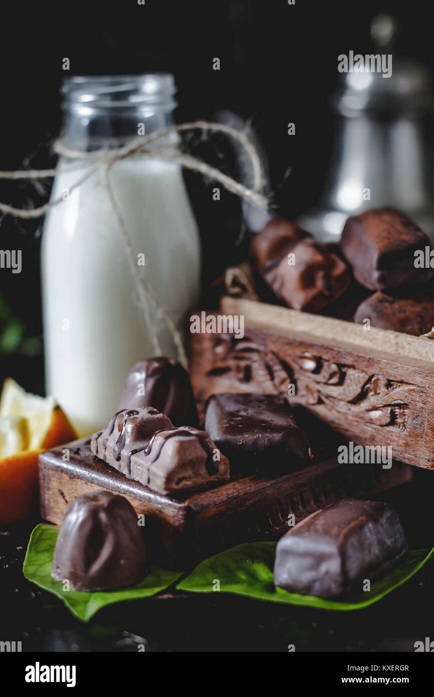 Milk in glass jar with orange and chocolate sweets. Dark wall at