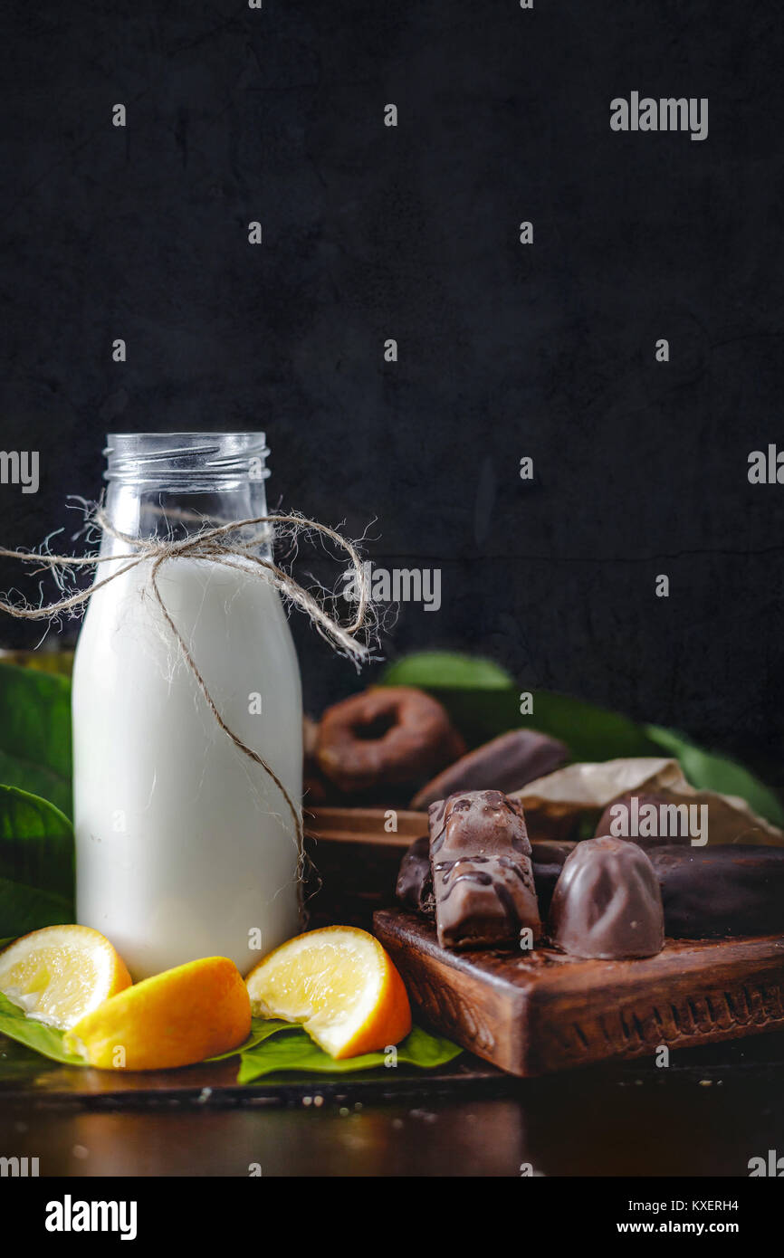 Milk in glass jar with orange and chocolate sweets. Dark wall at