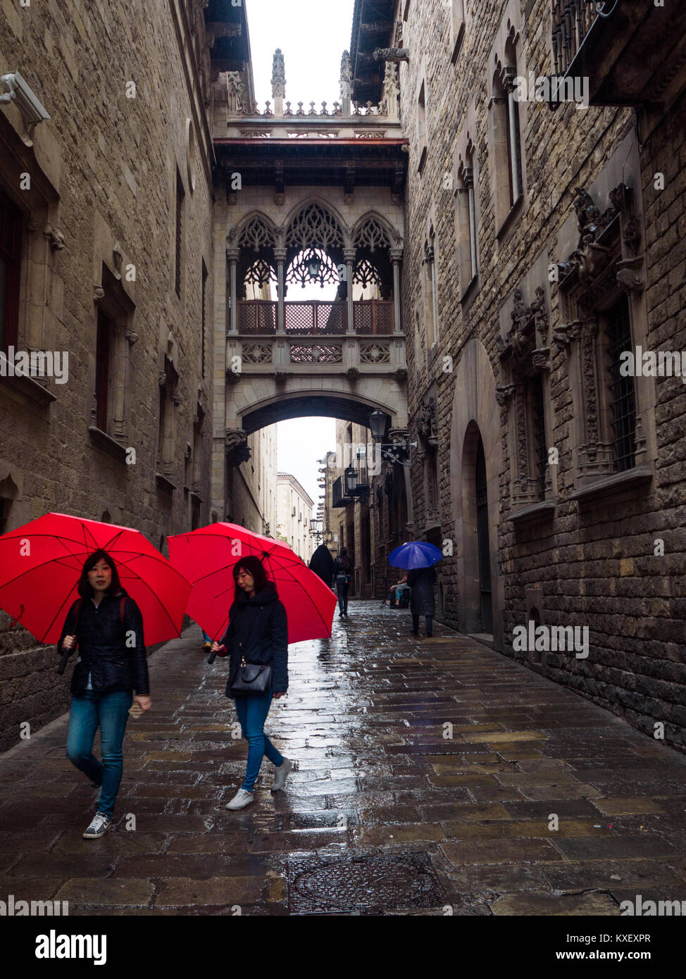 Two oriental tourist women walk through Barcelona Gothic Quartier, under the rain and the arch in Carrer del Bisbe (Bishop Street), carrying same red  Stock Photo