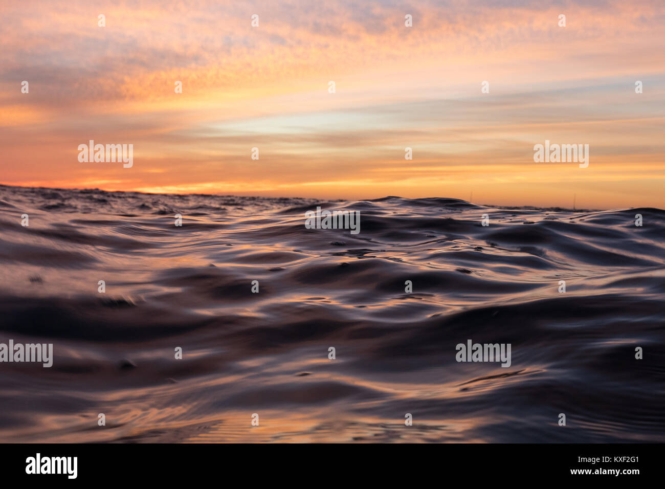Ripples extend across the surface of the ocean during a vibrant sunset afterglow in Los Angeles, California. Stock Photo