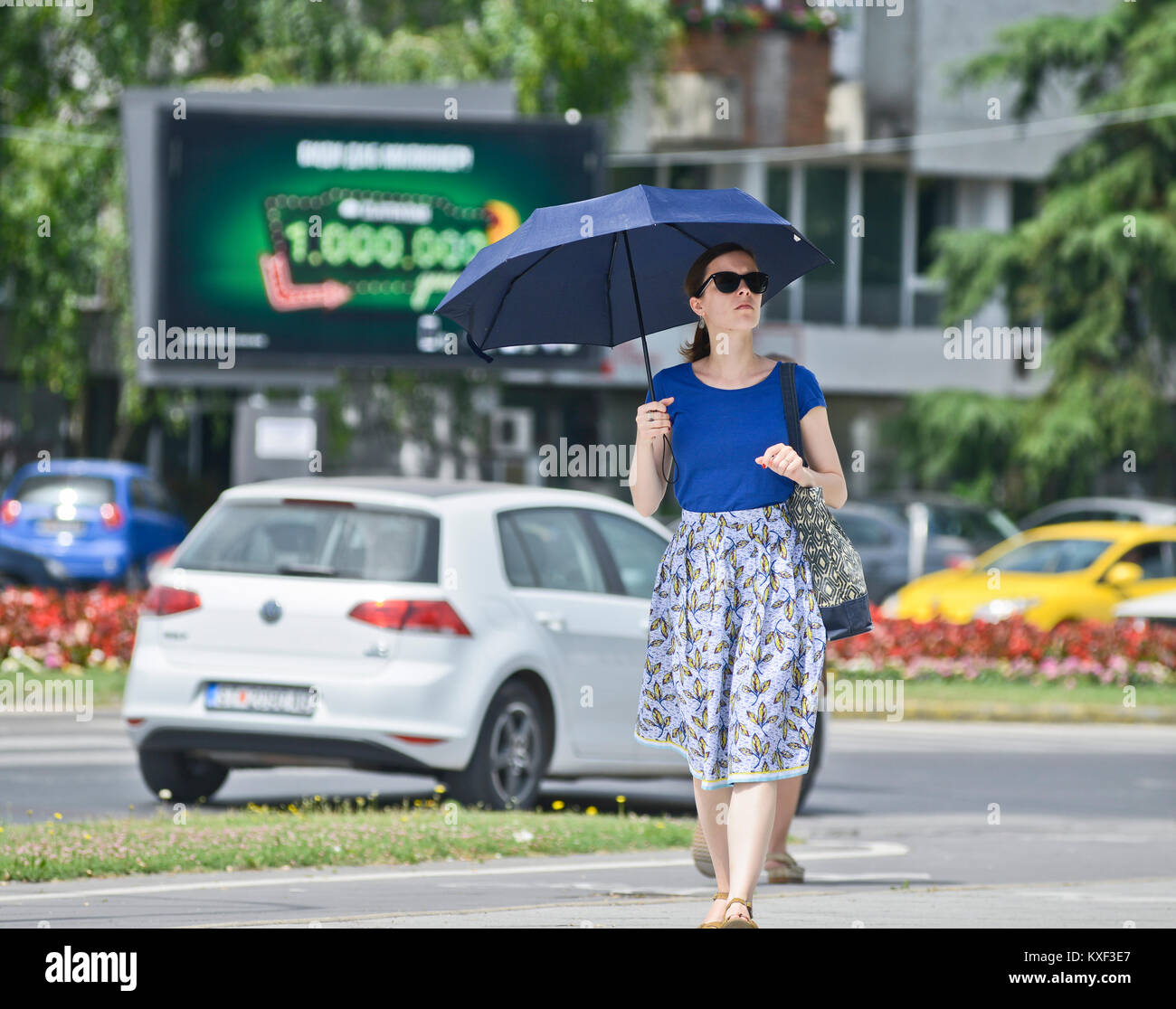 A woman walking under the sun with umbrella and sunglasses. Boulevard Ilinden, Skopje, Macedonia Stock Photo