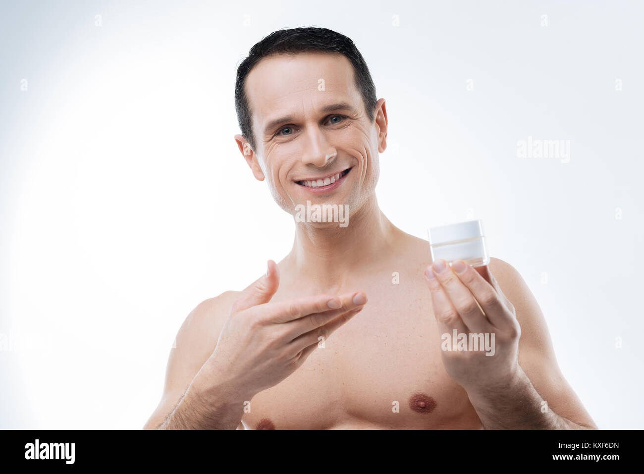 Cheerful pleasant man presenting facial cream Stock Photo