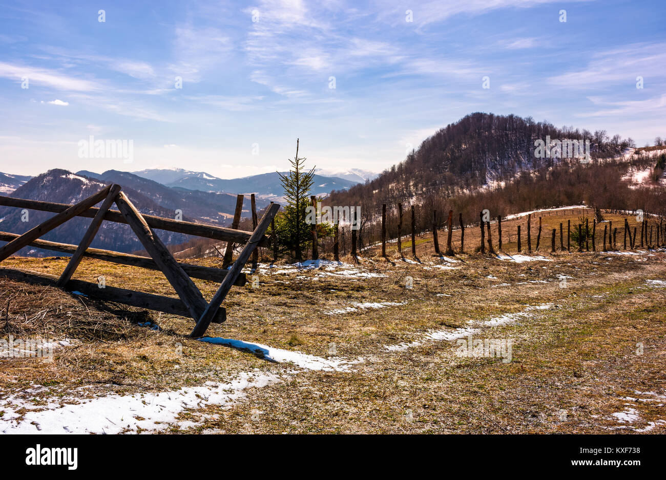 broken wooden fence on hillside. springtime is coming. beautiful mountainous landscape with some snow on slopes with weathered grass on a bright day Stock Photo