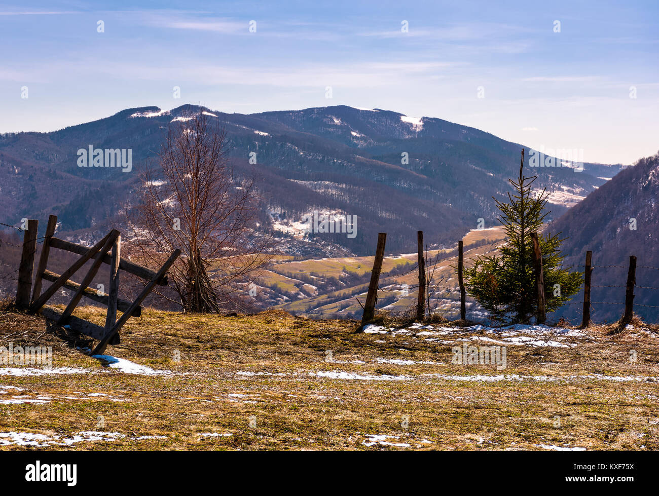 broken wooden fence on hillside. springtime is coming. beautiful mountainous landscape with some snow on slopes with weathered grass on a bright day Stock Photo