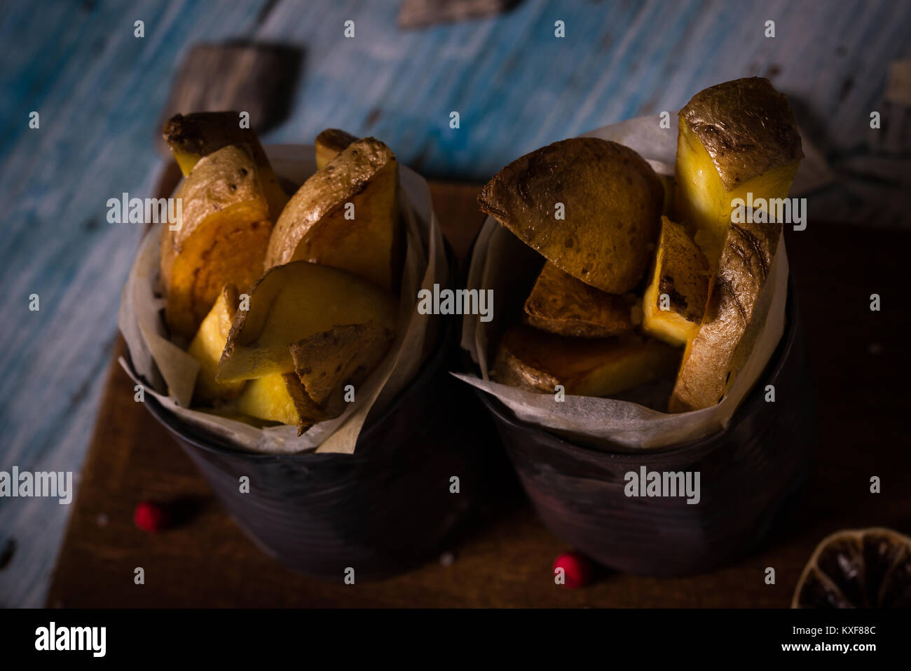 Horizontal photo on two vintage worn metal cans which are filled by paper sheet and roasted potato strips. Cans are on wooden board with worn blue and Stock Photo