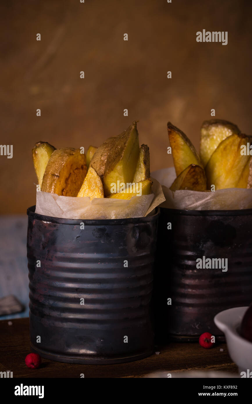 Vertical photo on two vintage worn metal cans which are filled by paper sheet and roasted potato strips. Cans are on wooden board with worn blue and w Stock Photo
