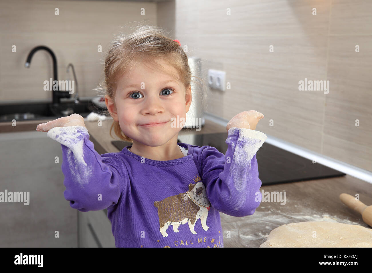 Happy little girl with dirty sleeves in flour. Funny home portrait of smiling child. Stock Photo