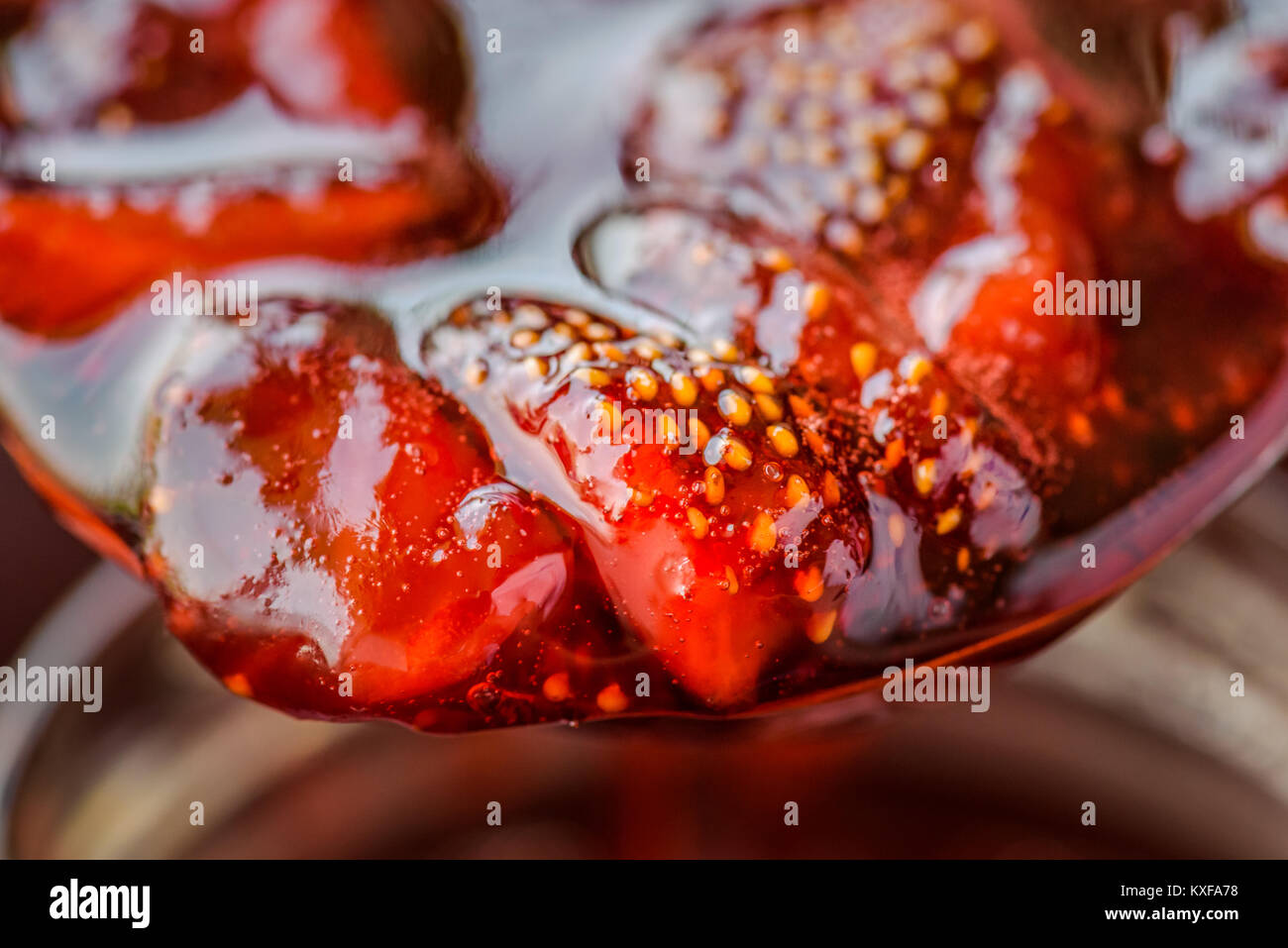 Close up of a spoon with delicious fresh homemade strawberry sauce above a jar. Stock Photo
