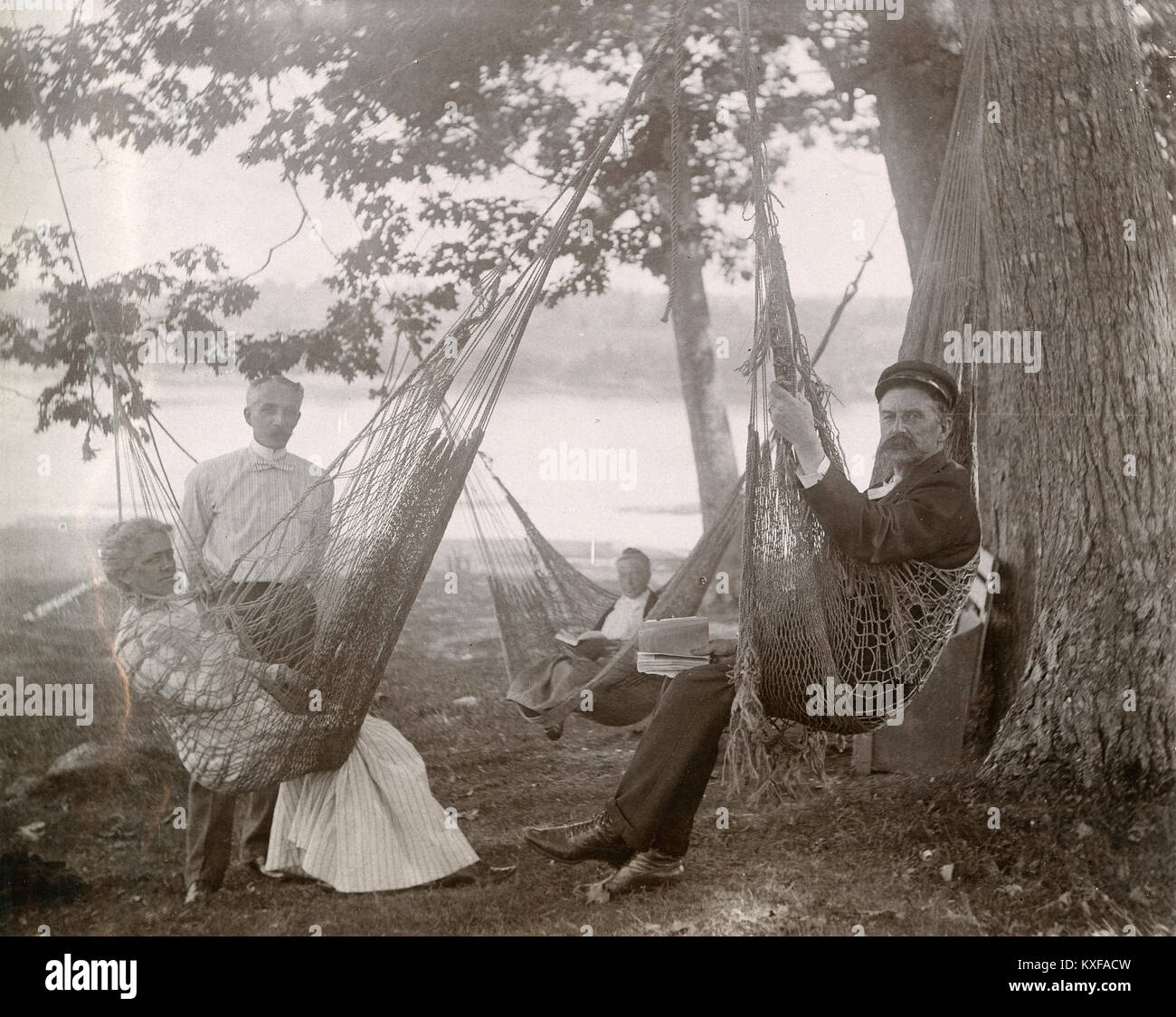 Antique circa 1905 photograph, family resting in a shady glen with bench and hammocks, with the Sasanoa River behind them. Location is in or near Riggsville (now Robinhood), Maine in Sagadahoc County, USA. Stock Photo