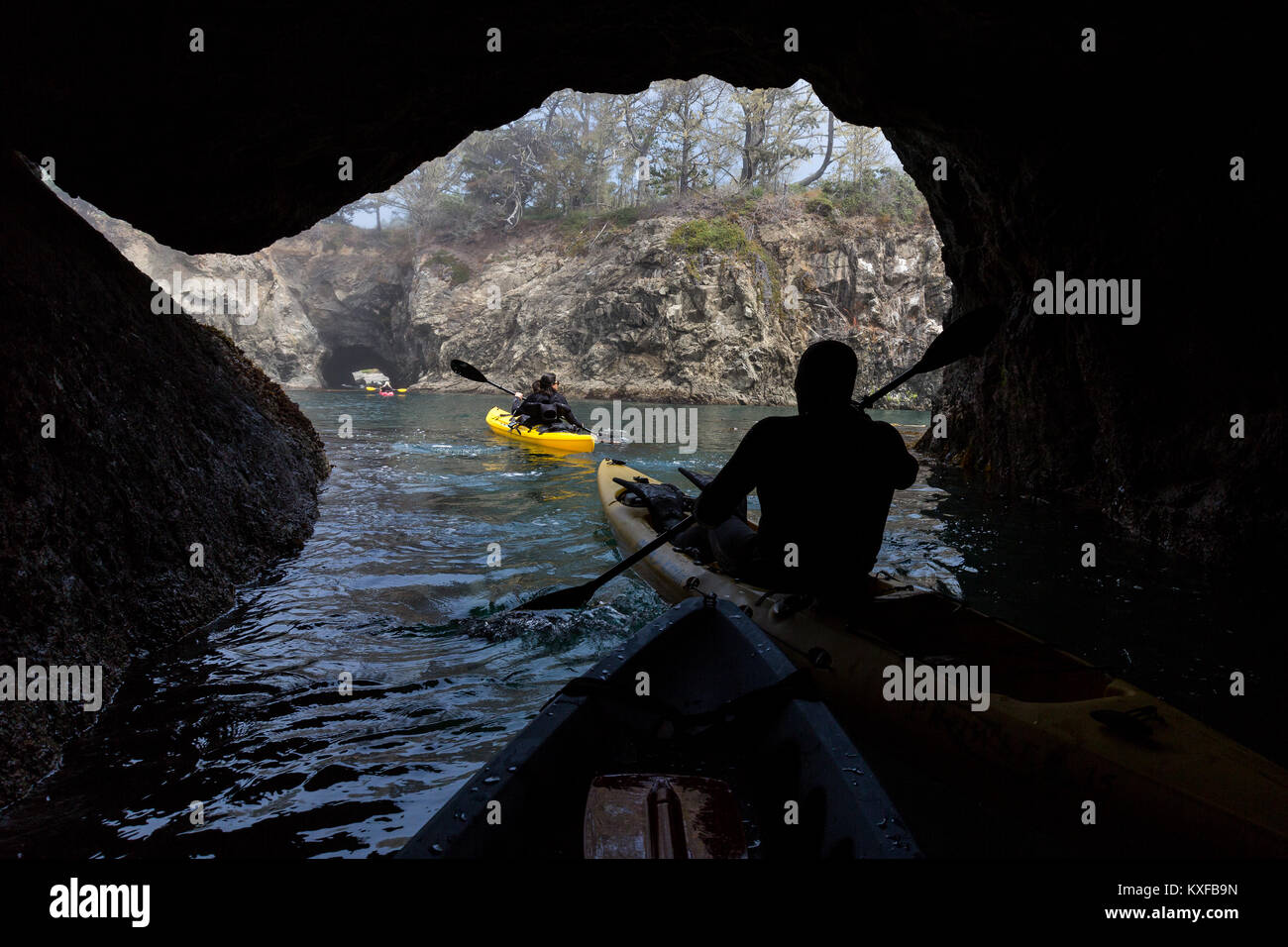 Sea kayakers in abalone diving wetsuits paddle through a sea cave near Russian Gulch State Park. Stock Photo