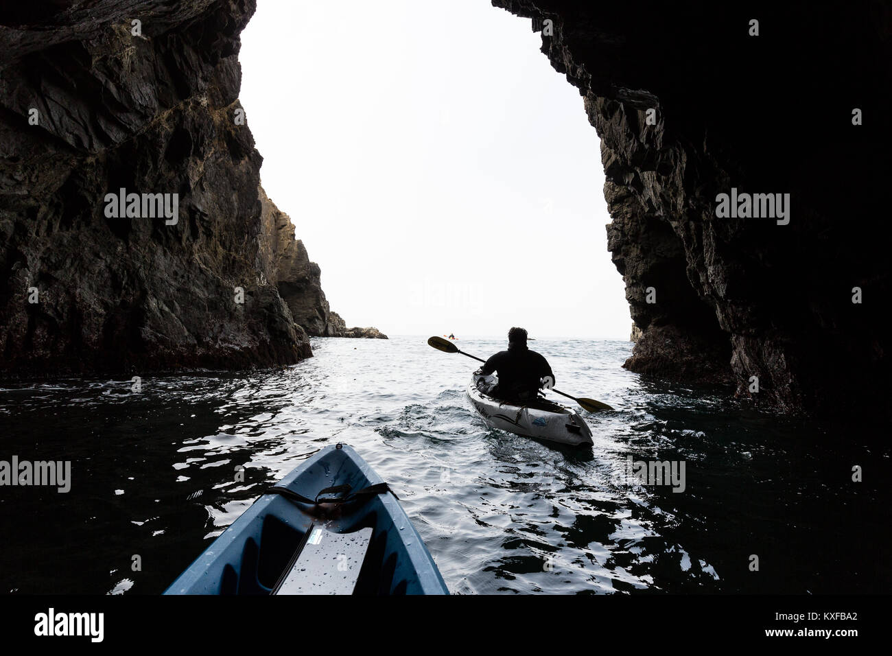 A sea kayaker in abalone diving wetsuits paddle through a sea cave near Russian Gulch State Park. Stock Photo