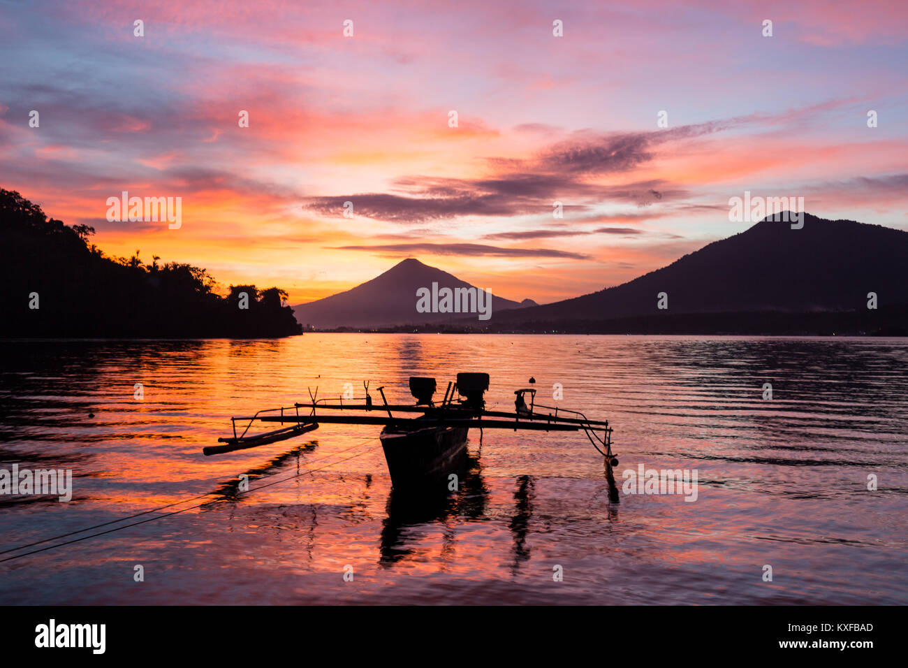 A junkong boat rests on calm water during a rich sunset afterglow in Indonesia's famed Lembeh Strait. Stock Photo
