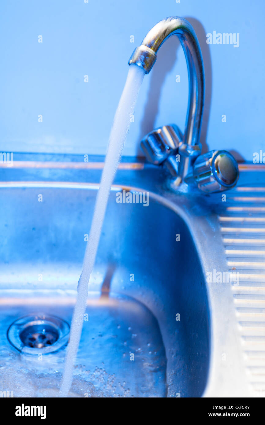 A stream of clean water flows into the stainless steel sink in blue