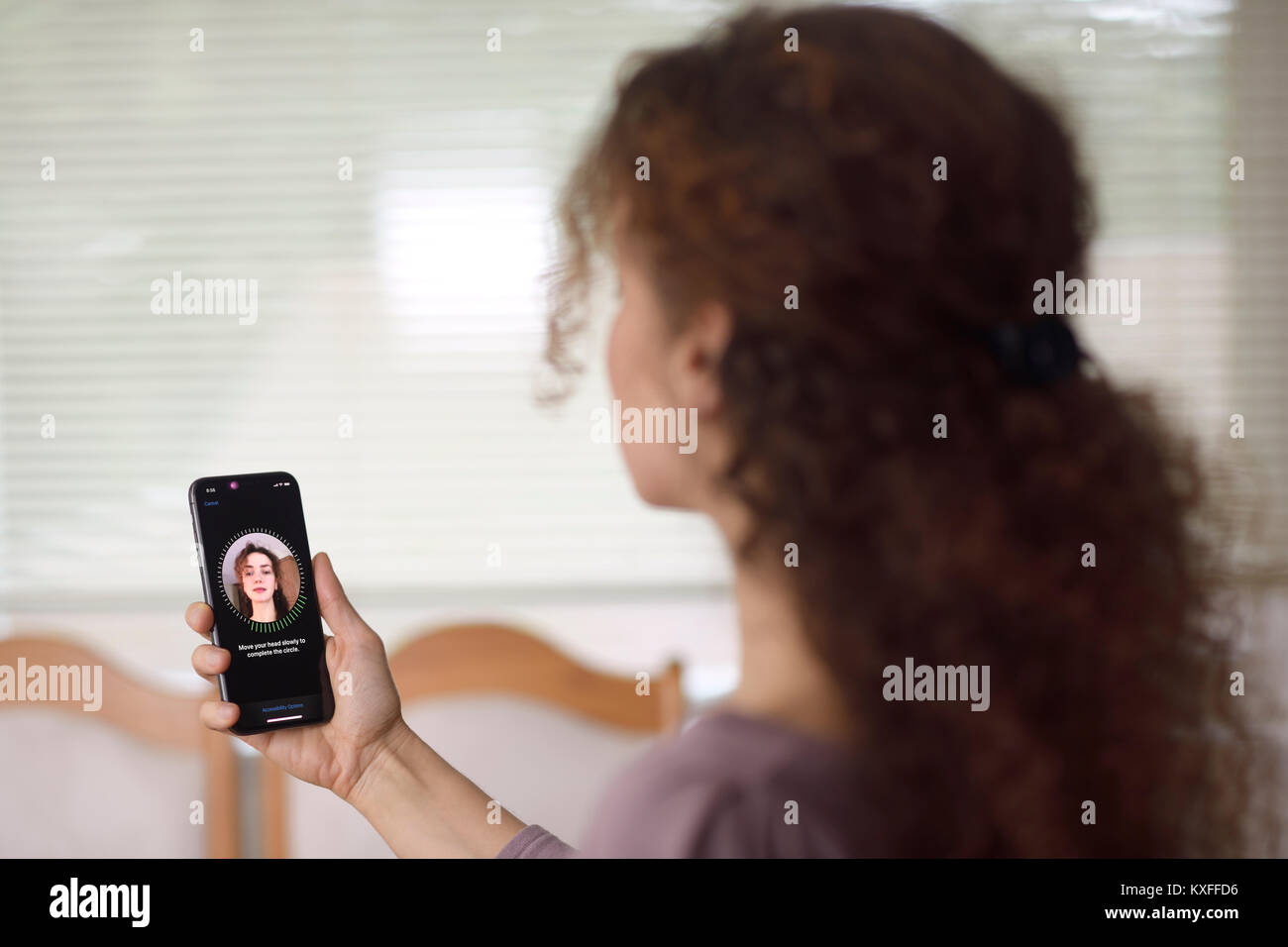 Woman with Apple iPhone X in her hand setting up Face ID, biometric authentication, by scanning her face with a new depth sensing camera from various  Stock Photo