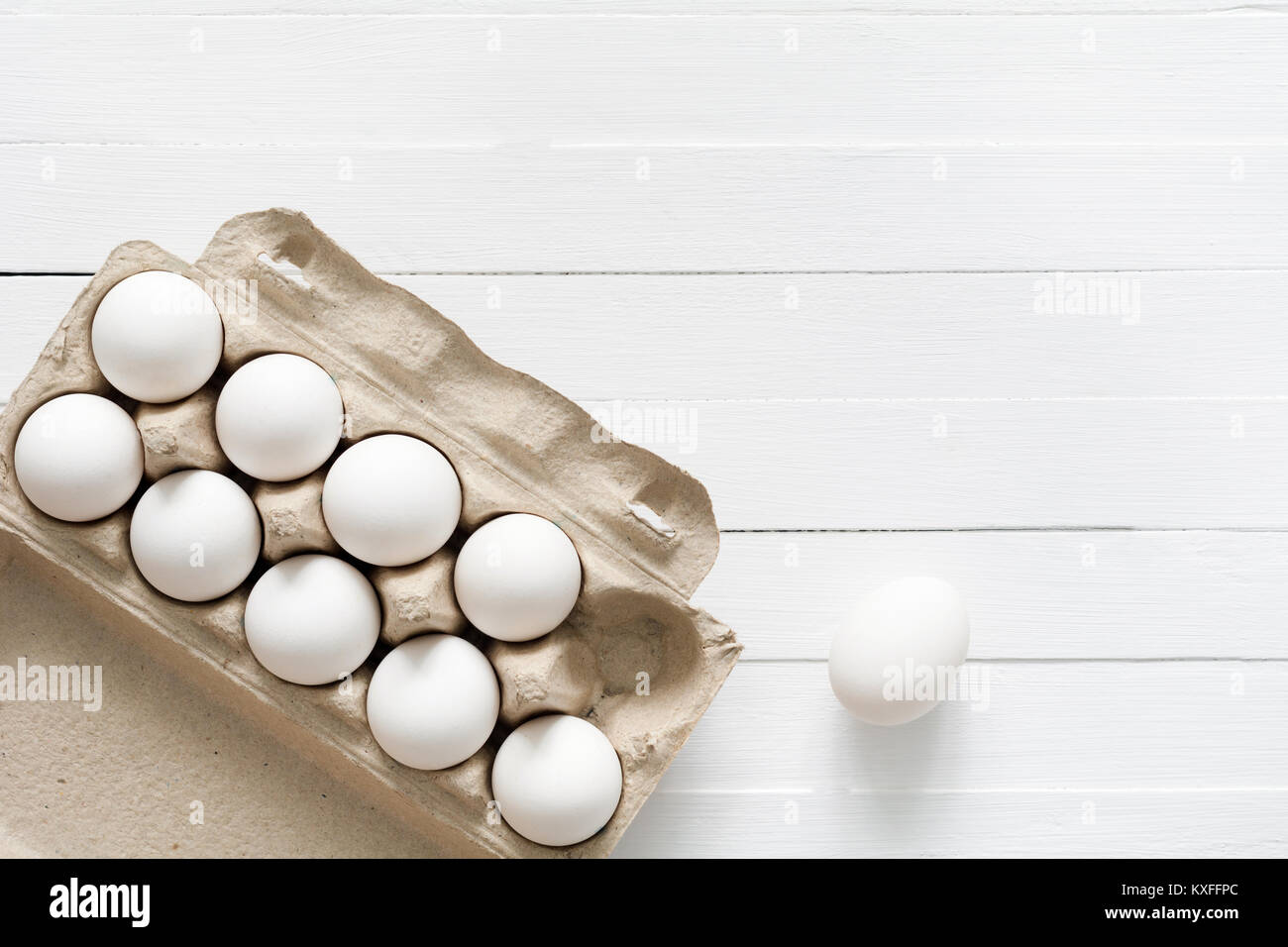 White eggs in carton box on white wooden background with copy space for text. Table top view Stock Photo