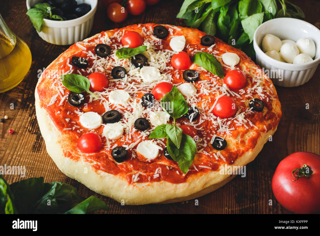 Homemade italian pizza with black olives, cherry tomatoes, cheese and basil on wooden board. Closeup view Stock Photo
