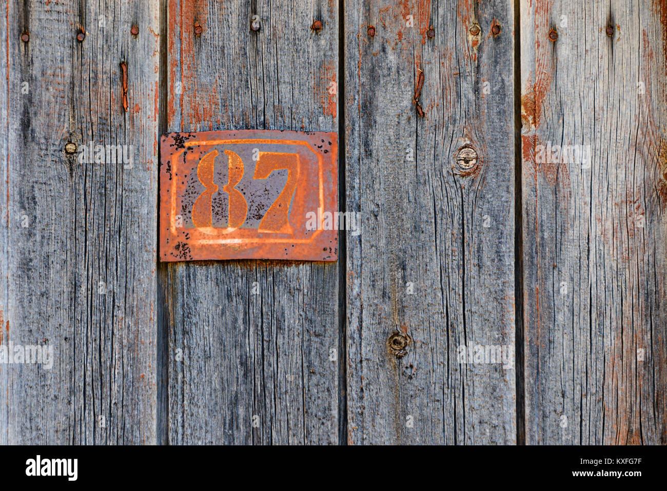 Rusty grunge metal house number plaque No. 87 on an old wooden door, vintage signs in Greece. Stock Photo