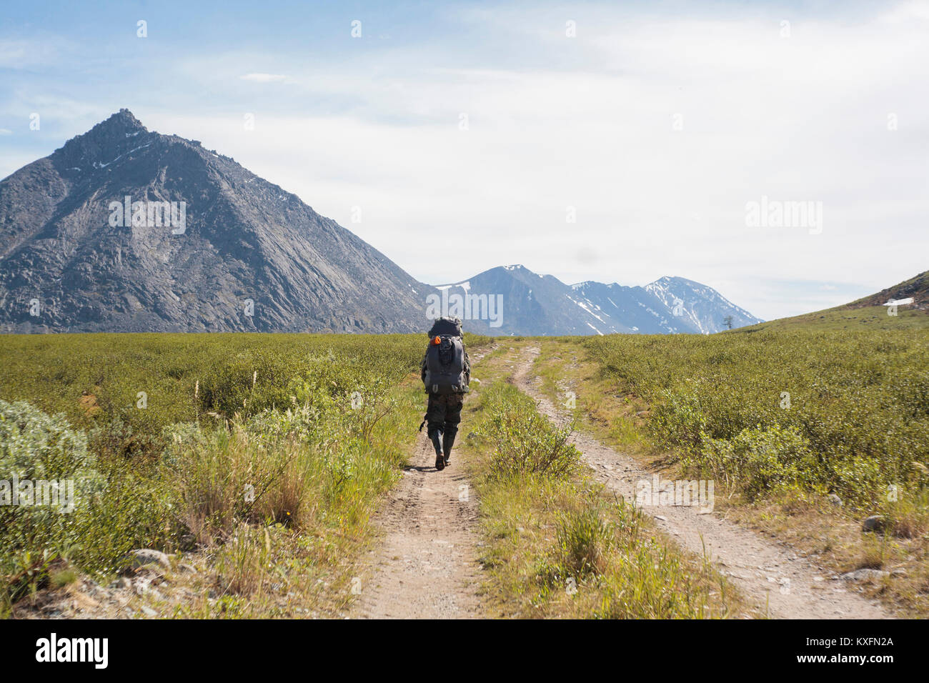 Rear view of male hiker walking on trail amidst field against sky Stock Photo