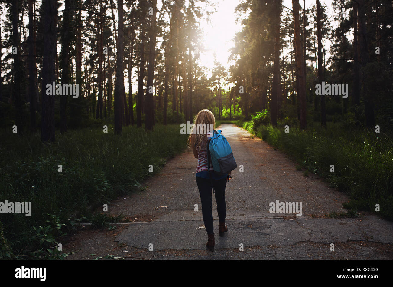 Rear view of woman with backpack walking on country road amidst trees ...