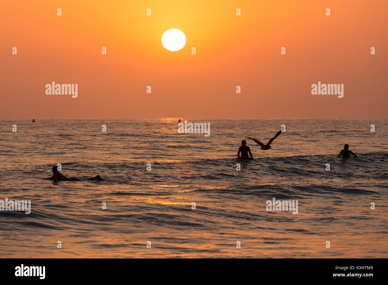 Surfers are silhouetted against the setting sun over the ocean in Los Angeles, California. Stock Photo