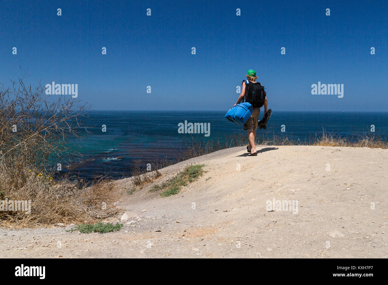 A diver carries gear down a dirt trail to the ocean in Southern California. Stock Photo