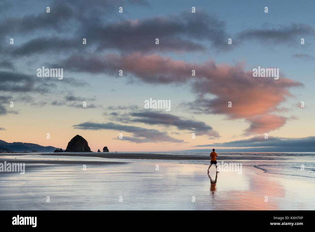 A man walks across the sand to shoot photos of Haystack Rock in Cannon Beach, Oregon. Stock Photo