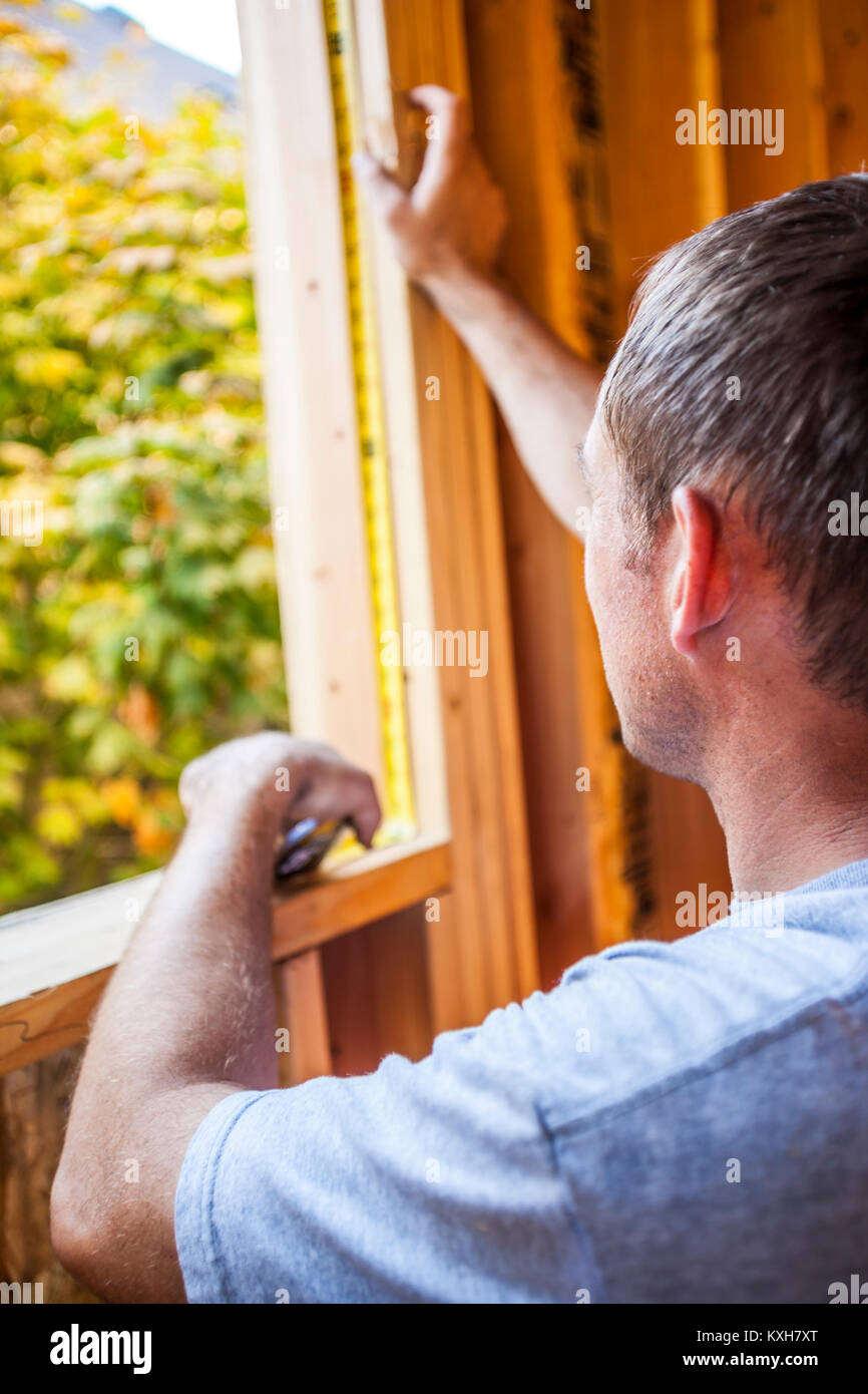 A man measuring the inside of a window frame on a residential house